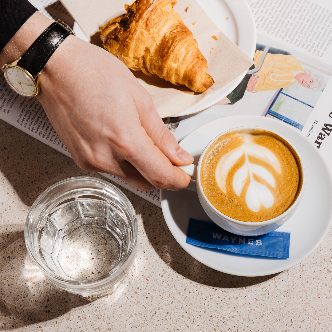 A croissant, a cappuccino and a glass of water on a café table